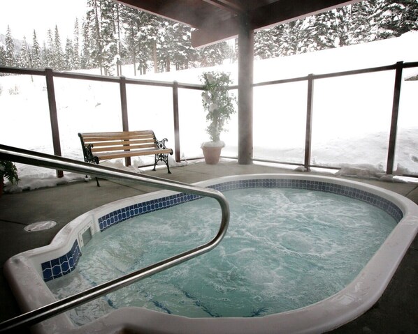 A hot tub with a tiled edge, a wooden bench, and a potted plant.