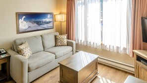 A cozy living room with a sofa, a coffee table, a painting of a snowy landscape, and a television on a wooden stand.