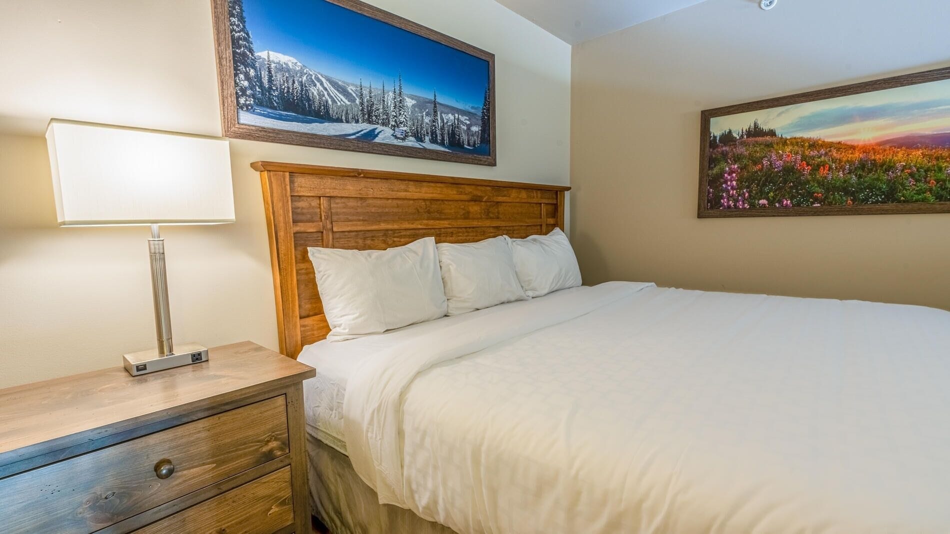 A neatly made bed with white linens, a wooden headboard, and a bedside table with a lamp.