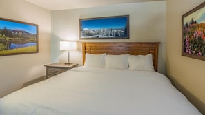 A hotel room with a large bed, a wooden headboard, a nightstand with a lamp, and two framed pictures on the walls.