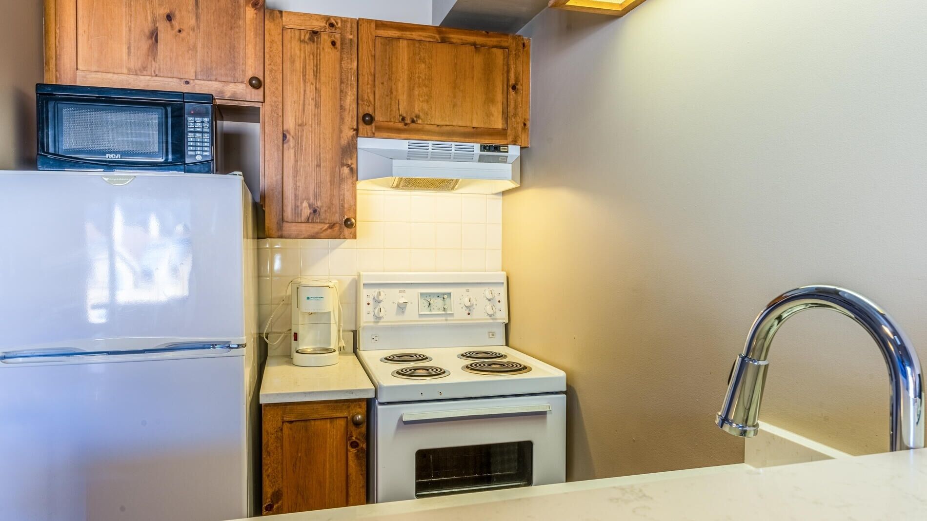A compact kitchen with a refrigerator, microwave, coffee maker, stove, and wooden cabinets.