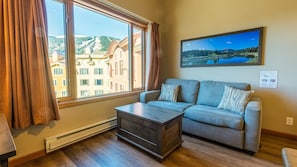 A modern living room with a sofa, a coffee table, and a large window offering a view of buildings and a lake.