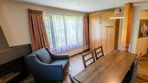 A dining area with a wooden table, two chairs, a blue sofa, a wooden cabinet, and a window with curtains.
