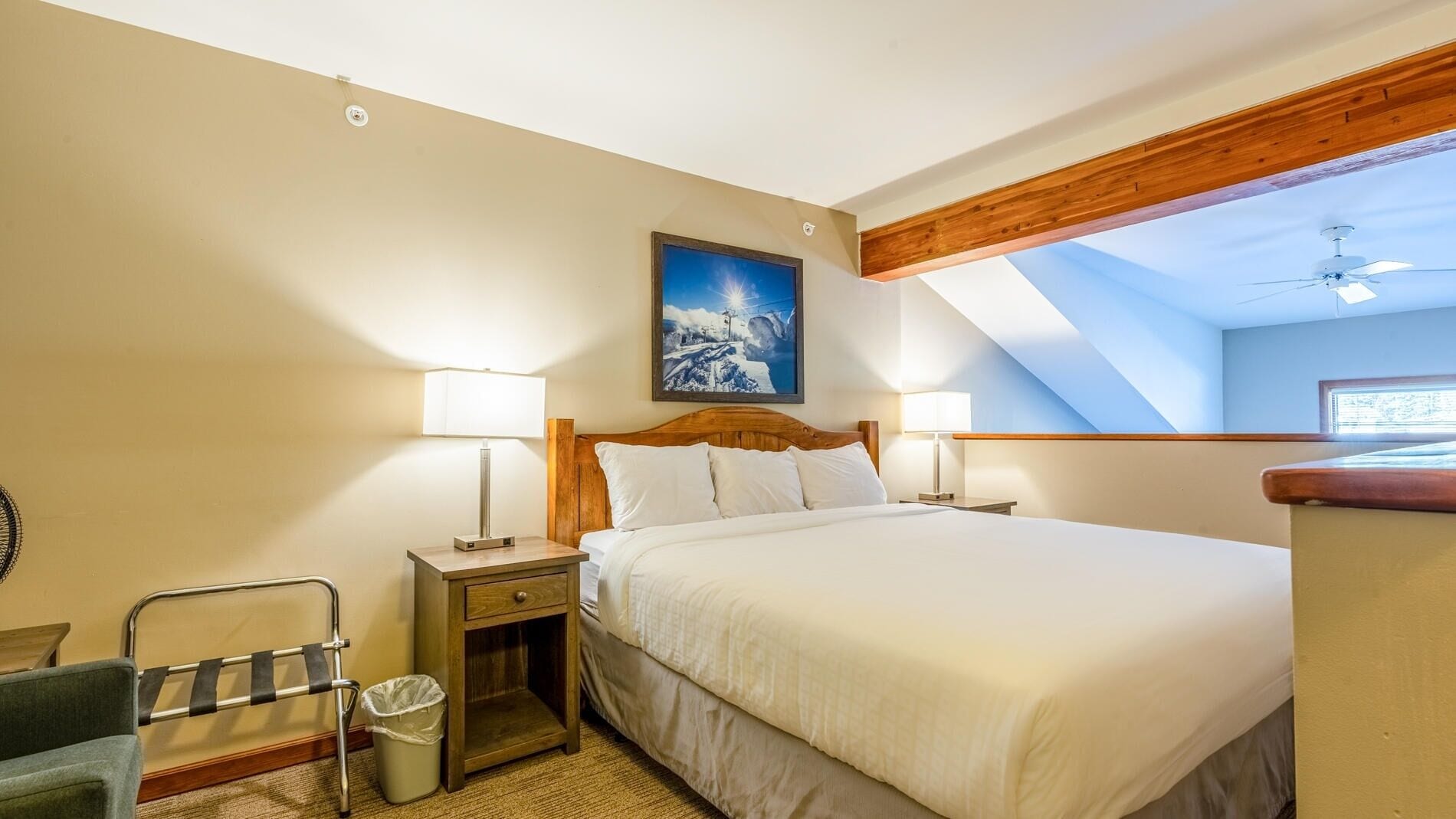 A bedroom with a large bed, two bedside tables with lamps, a wooden headboard, a ceiling fan, and a skylight.