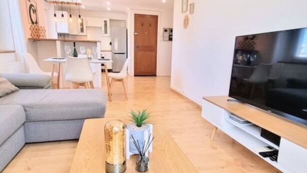 A modern living room with a sectional sofa, a flat-screen TV, and a wooden coffee table with decorative items. - Le Barbusse Coeur de Ville Superbe Déco Climatisé (Sète)
