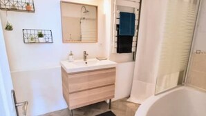 A modern bathroom with a white sink, wooden vanity, and a bathtub. - Le Barbusse Coeur de Ville Superbe Déco Climatisé (Sète)