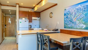 A compact kitchen with wooden cabinets, a white refrigerator, a stove, and a dining area with a table and chairs.
