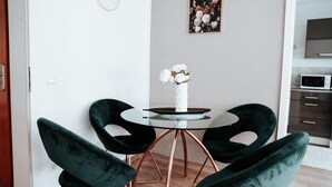 A dining area with a round table, four dark green chairs, a vase with white flowers, a clock, and a floral painting on the wall. - Apartment "Ella 1" with Lake View, Balcony and Wi-Fi (Friedrichshafen)