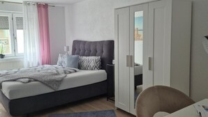 A bedroom with a bed, a desk, a chair, a wardrobe, and a window with curtains. - Apartment "Ella 1" with Lake View, Balcony and Wi-Fi (Friedrichshafen)