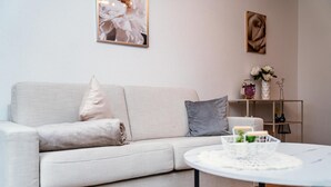 Een woonkamer met een bank, een ronde tafel, een klein rekje met decoratieve objecten, en wanddecoratie.