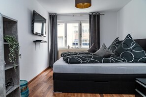 A bedroom with a bed, a TV mounted on the wall, a window with curtains, and a plant on a shelf. - Apartment 'Ella 2' with Lake View, Balcony and Wi-Fi (Friedrichshafen)