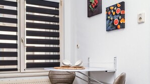 Een hoekappartement met raam, twee stoelen, een tafeltje en twee schilderijen aan de muur.