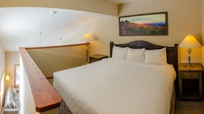 A bedroom with a large bed, a wooden bench, two bedside tables with lamps, and a painting on the wall. - Cahilty #364 Hotel Room (Sun Peaks)