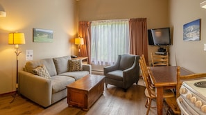 A cozy living room with a sofa, armchair, wooden coffee table, and dining table.