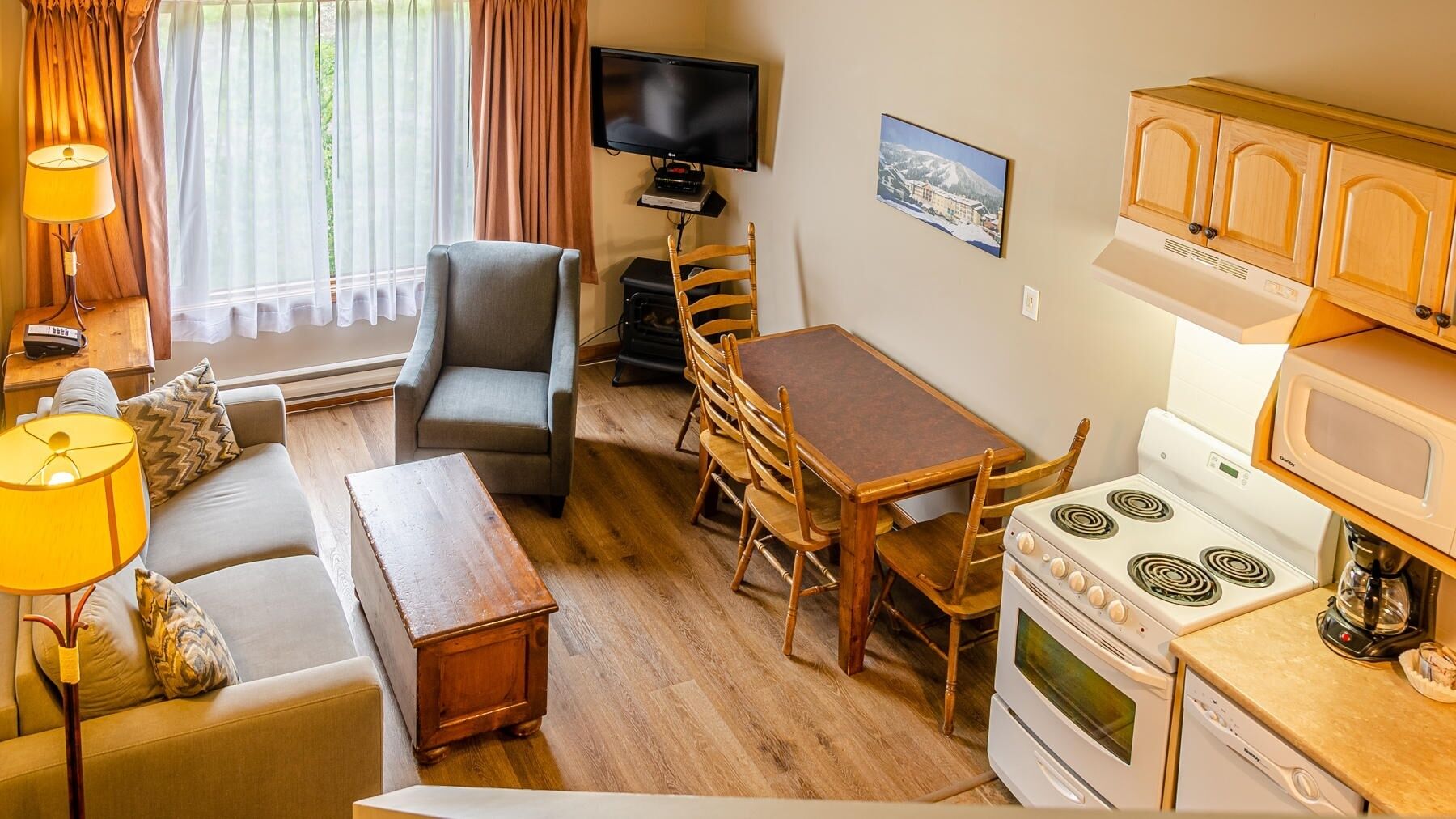 Ein kompakter Wohnraum mit Sofa, Sessel, Esstisch und einer Küchenzeile mit Herd und Mikrowelle.