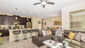 Ein modernes Wohnzimmer mit grauem Sofa, einem Couchtisch und einer Essecke mit Barhocker.
