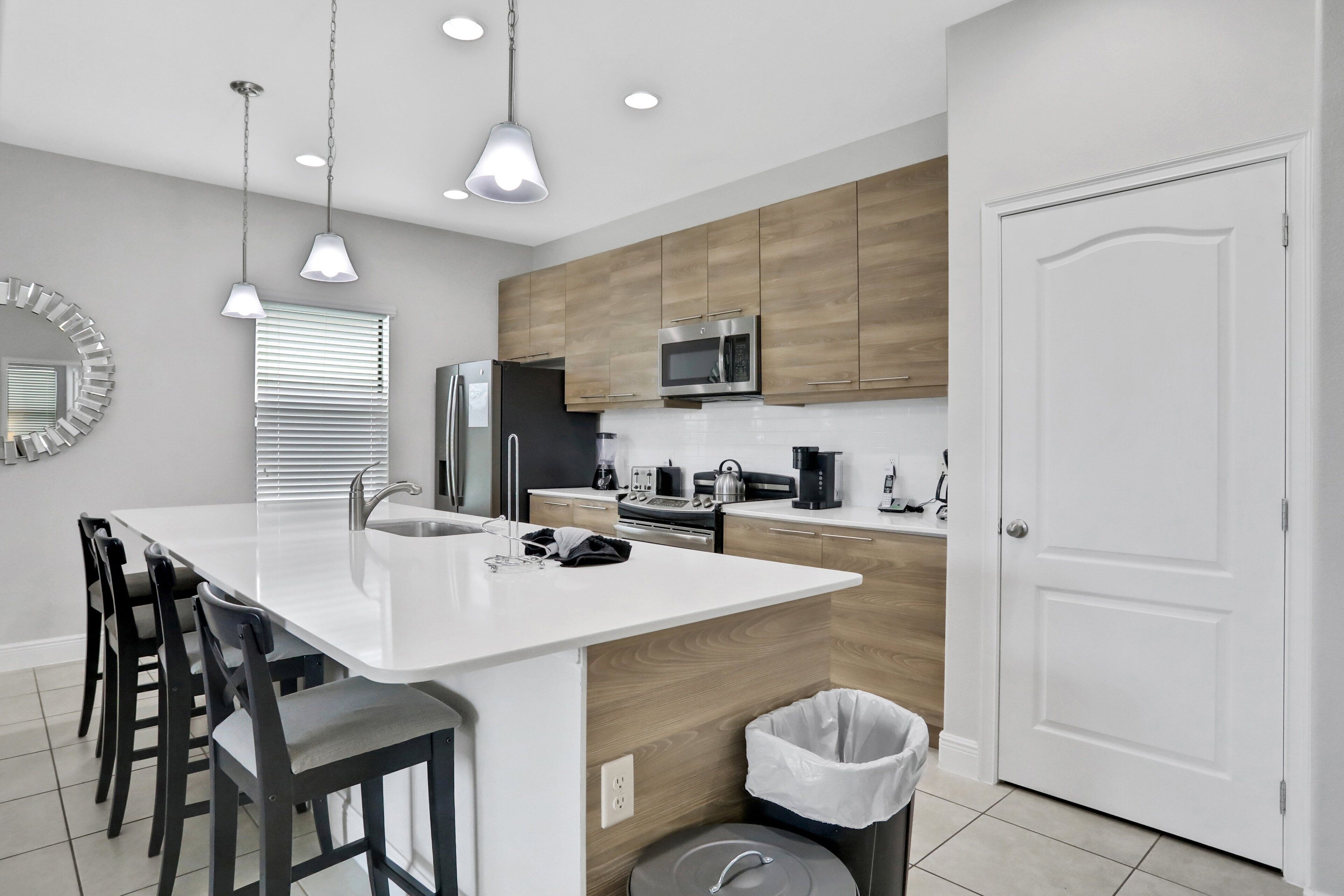 A modern kitchen with a central island, wooden cabinets, stainless steel appliances, and a white door.