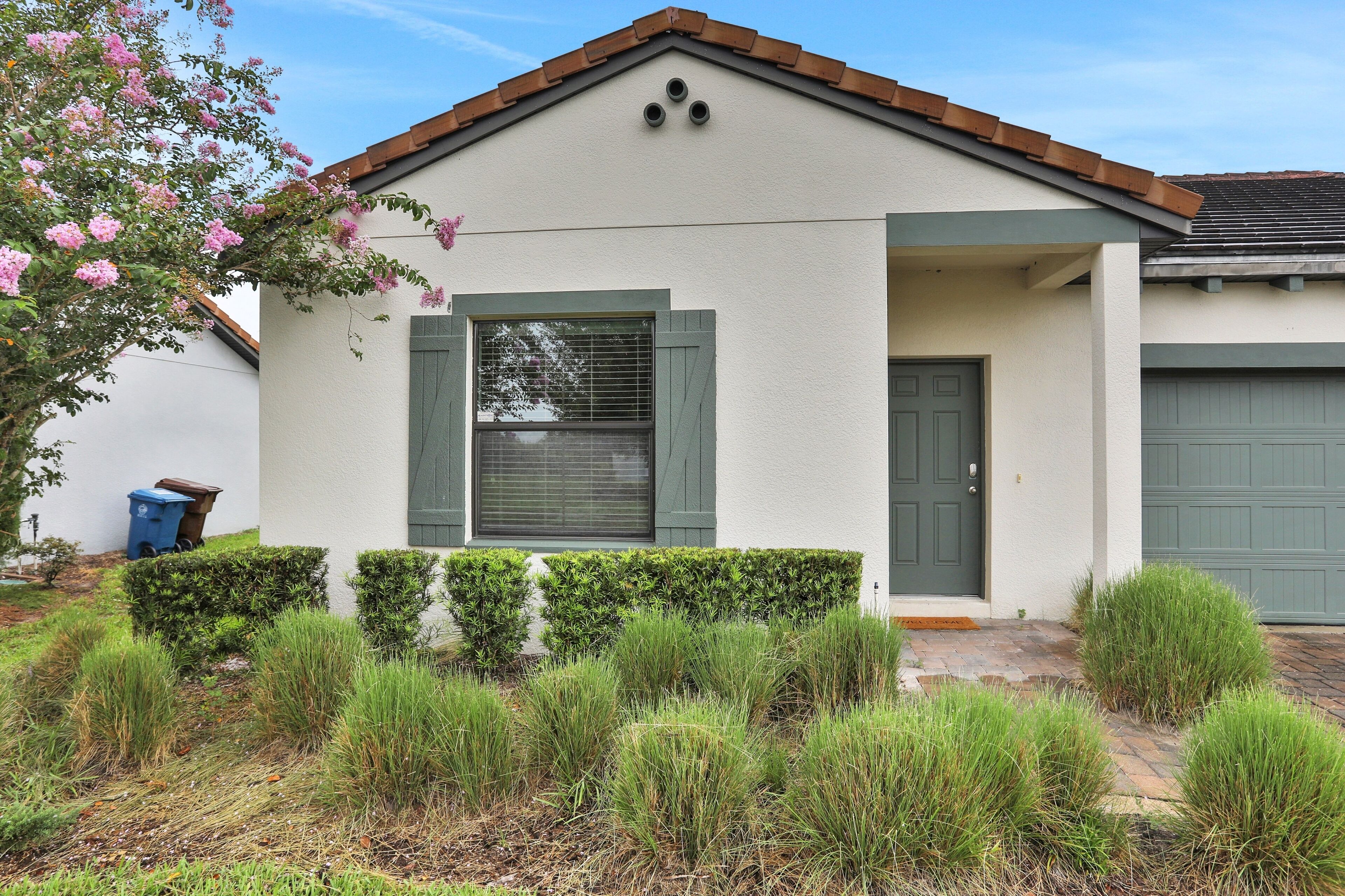 A single-story house with a front porch, a green door, and a window with shutters.