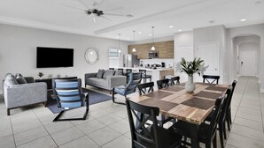 Ein modernes Wohnzimmer mit grauem Sofa, blauen und schwarzen Sesseln, einem Holzessttisch und einer Küche im Hintergrund.