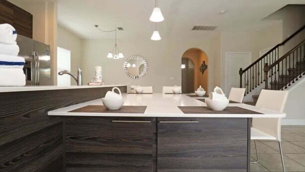 Una cucina moderna con isola centrale, sedie bianche e una scala che conduce a un altro piano.