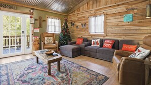 A cozy cabin interior with a wooden interior, a Christmas tree, leather furniture, and a rustic ceiling. - Creekbend 3 Bedroom Home (Sevierville)