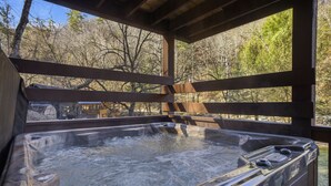 A hot tub under a wooden pergola with a view of trees and a cabin in the background. - Creekbend 3 Bedroom Home (Sevierville)