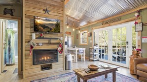 A cozy living room with a fireplace, wooden walls, a large window, and a Tennessee sign. - Creekbend 3 Bedroom Home (Sevierville)