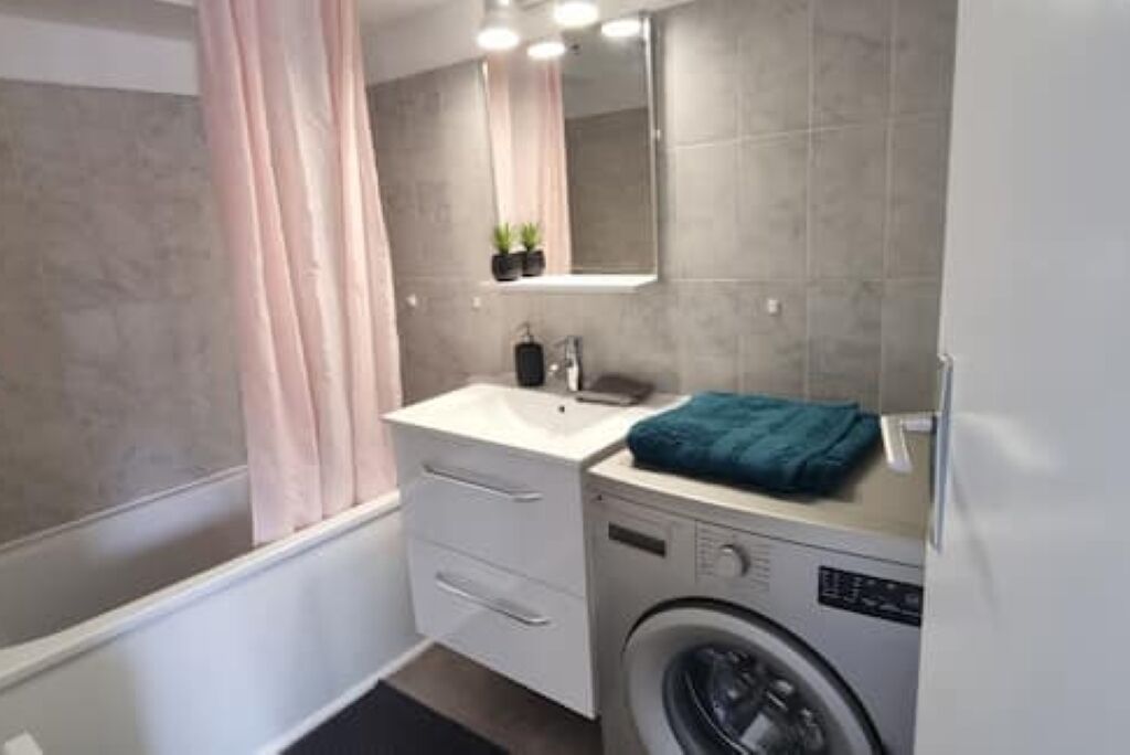 A compact bathroom with a washing machine, a sink, and a mirror.