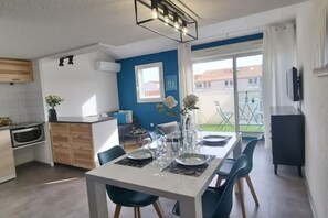 Une cuisine moderne avec des meubles blancs, un coin repas avec une table dressée pour deux personnes, et une vue sur l’extérieur.