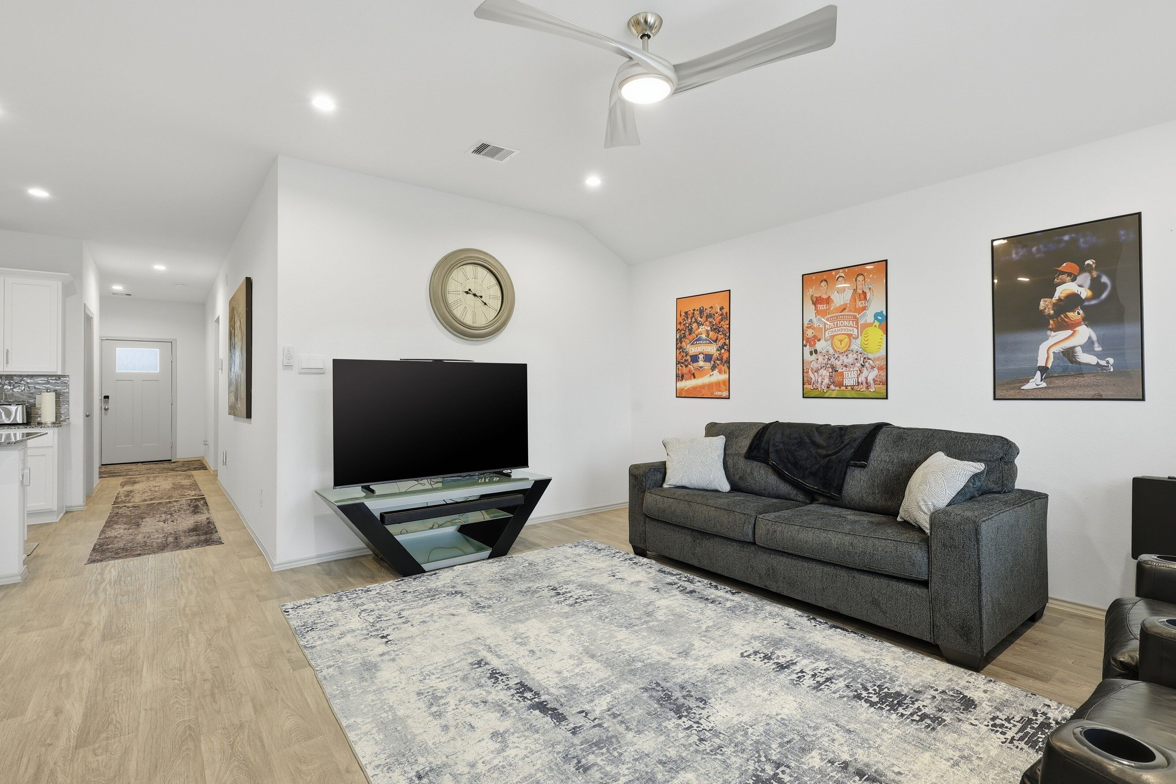 A modern living room with a flat-screen TV, grey sofa, and a ceiling fan.