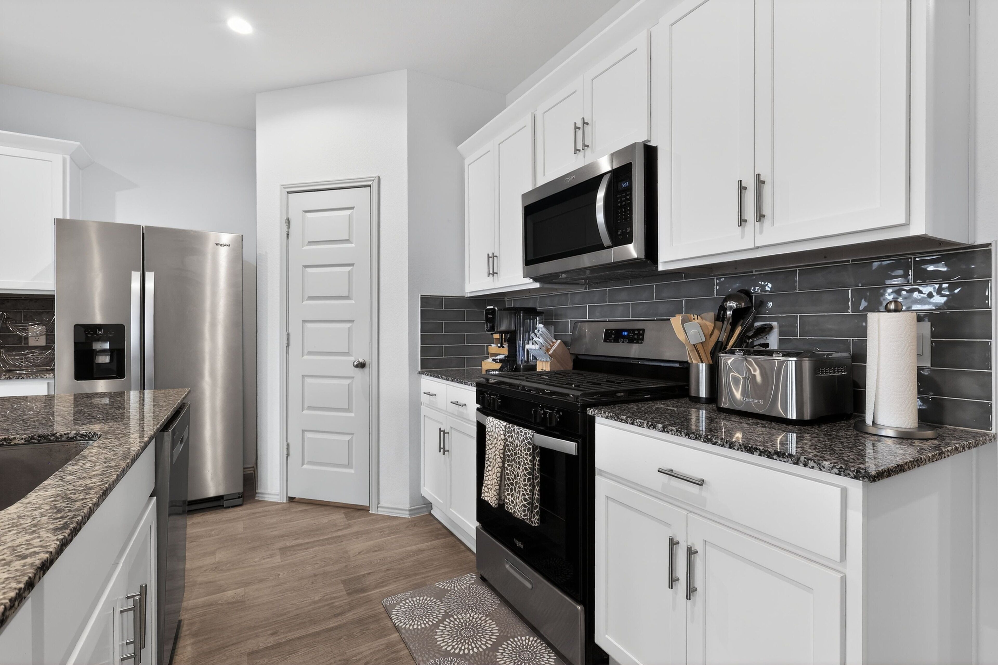 A modern kitchen with stainless steel appliances, white cabinetry, and a granite countertop.