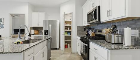 A modern kitchen with white cabinets, stainless steel appliances, and granite countertops.