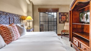 Una habitación de hotel con una cama grande, un armario de madera, una silla y una ventana con vista a árboles.
