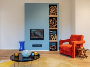 A living room with a blue wall, a fireplace, a red armchair, a small table with candles, and a glass bowl on a black table. - Cuadrat by Interhome (Isola d'Asti)