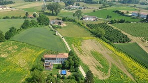 Luchtbeeld van een landelijk gebied met velden, een groot huis met een zonnepaneel en een stad in de verte.