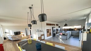Een moderne keuken met een centraal eiland, een eetgedeelte met een zwarte tafel, en een woonkamer met een bank en televisie.