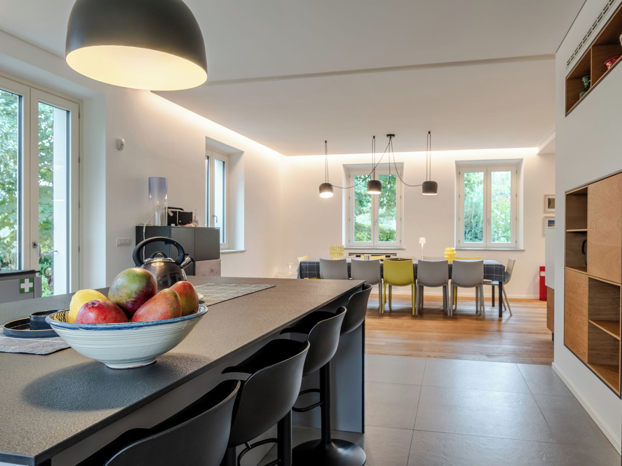 A modern kitchen with a central island, bar stools, pendant lighting, and a dining area with a table and chairs.