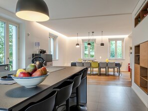 Una cocina moderna con una isla central, taburetes de bar, iluminación colgante y un comedor con mesa y sillas.