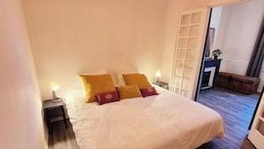 A bedroom with a large bed, two bedside tables with lamps, a wooden floor, and a door leading to another room. - LE PARC Authentique Coeur de Ville Prox Park CLIM (Sète)