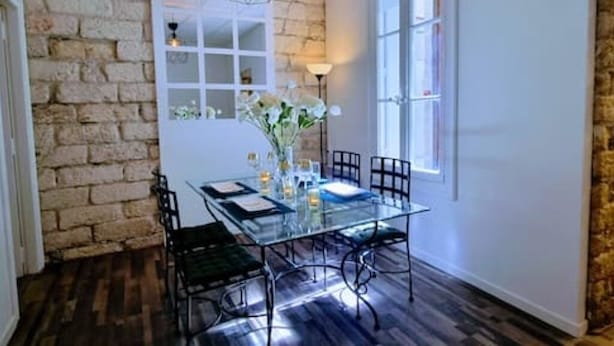 A dining area with a glass table, black chairs, a vase with flowers, and a stone wall. - LE PARC Authentique Coeur de Ville Prox Park CLIM (Sète)