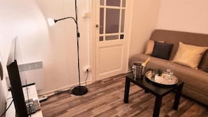 A living room with a sofa, a coffee table with a tray, a floor lamp, and a door. - LE PARC Authentique Coeur de Ville Prox Park CLIM (Sète)