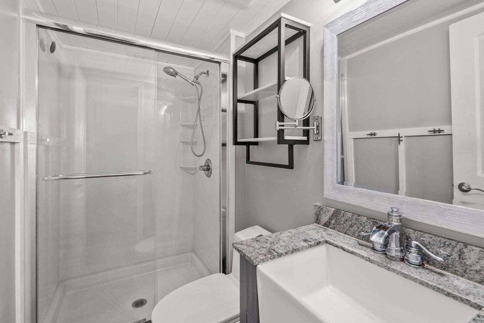 A modern bathroom with a glass-enclosed shower, a vanity with a granite countertop, and a large mirror above the sink.