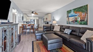 A modern living room with a sectional sofa, a dining area, and a kitchen in the background. - Sea Cloisters 101e 3 Bedroom Condo (North Myrtle Beach)