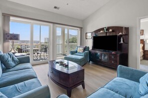 A spacious living room with a large TV, comfortable seating, and a balcony with a view. - Ocean Keyes 2445 3 Bedroom Condo (North Myrtle Beach)