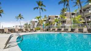 A swimming pool with lounge chairs and palm trees, surrounded by a building with balconies. - Big Island Alii Villas 225 1 Bedroom Condo (Kailua-Kona)