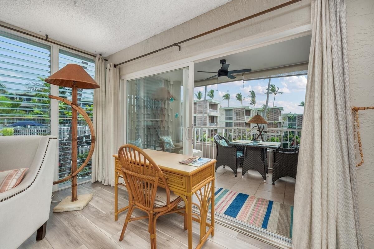 A balcony with a table and chairs, a floor lamp, and a view of a residential area with palm trees.