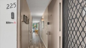 A hallway with a 'No Smoking' sign, a door with the number 225, and a view into a room with a table and chairs. - Big Island Alii Villas 225 1 Bedroom Condo (Kailua-Kona)
