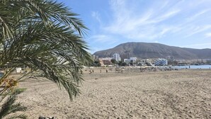 Una playa con una montaña al fondo, palmeras y edificios.