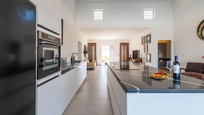 A modern kitchen with a central island, a dining area with a long table, and a living space with a sofa and artwork. - Charming 2-bedroom villa with AC in peaceful Grote Berg (Grote Berg)