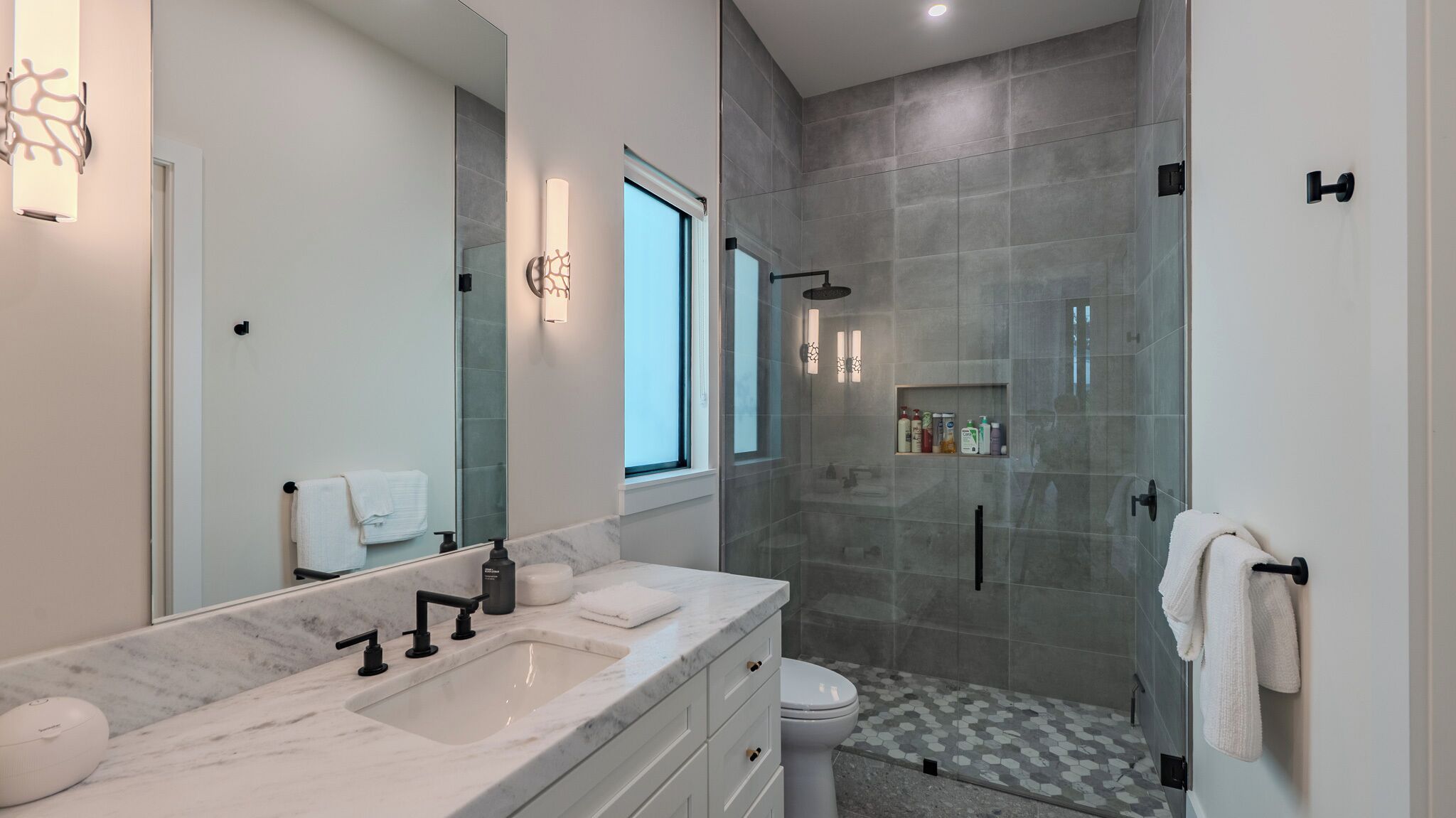 Un baño moderno con un espejo grande, un lavabo de mármol, un inodoro y una ducha a ras de suelo con puerta de cristal.